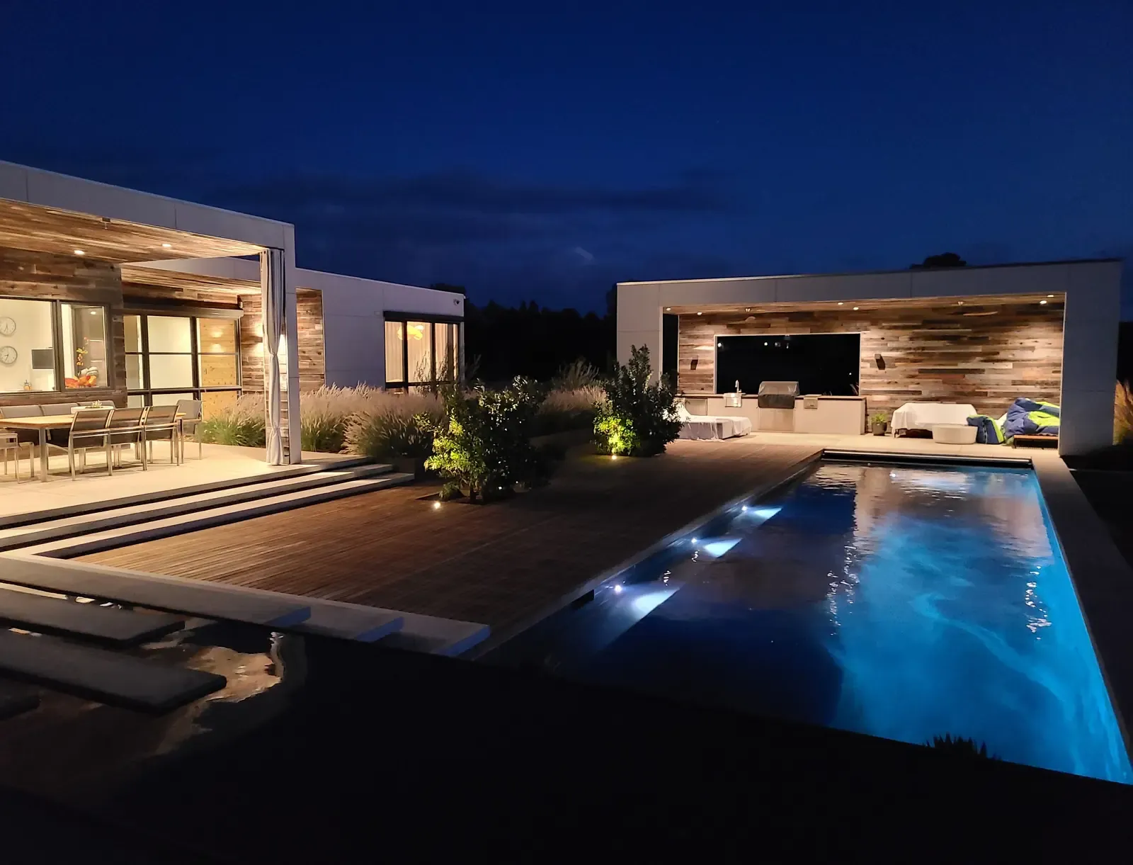 Pool glowing blue beside the timber deck, house and terrace lit behind