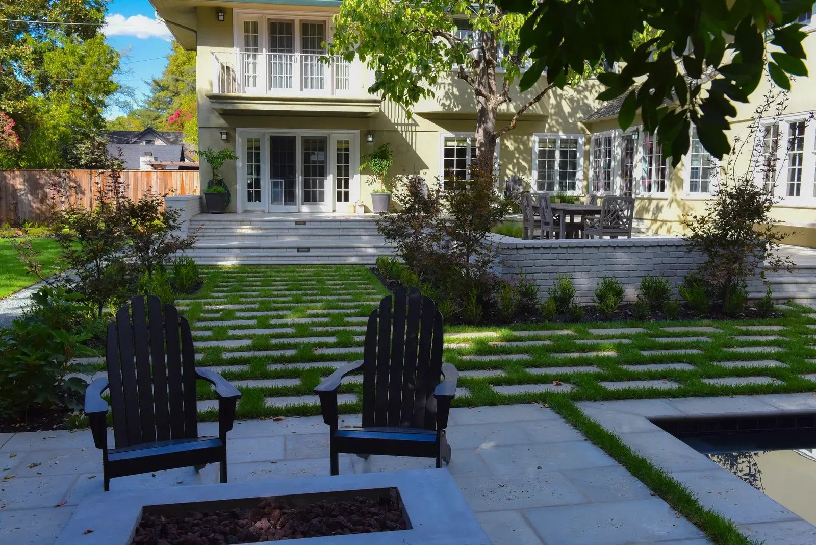 Adirondack chairs on the paved terrace, clipped hedging and lawn strips leading to the house