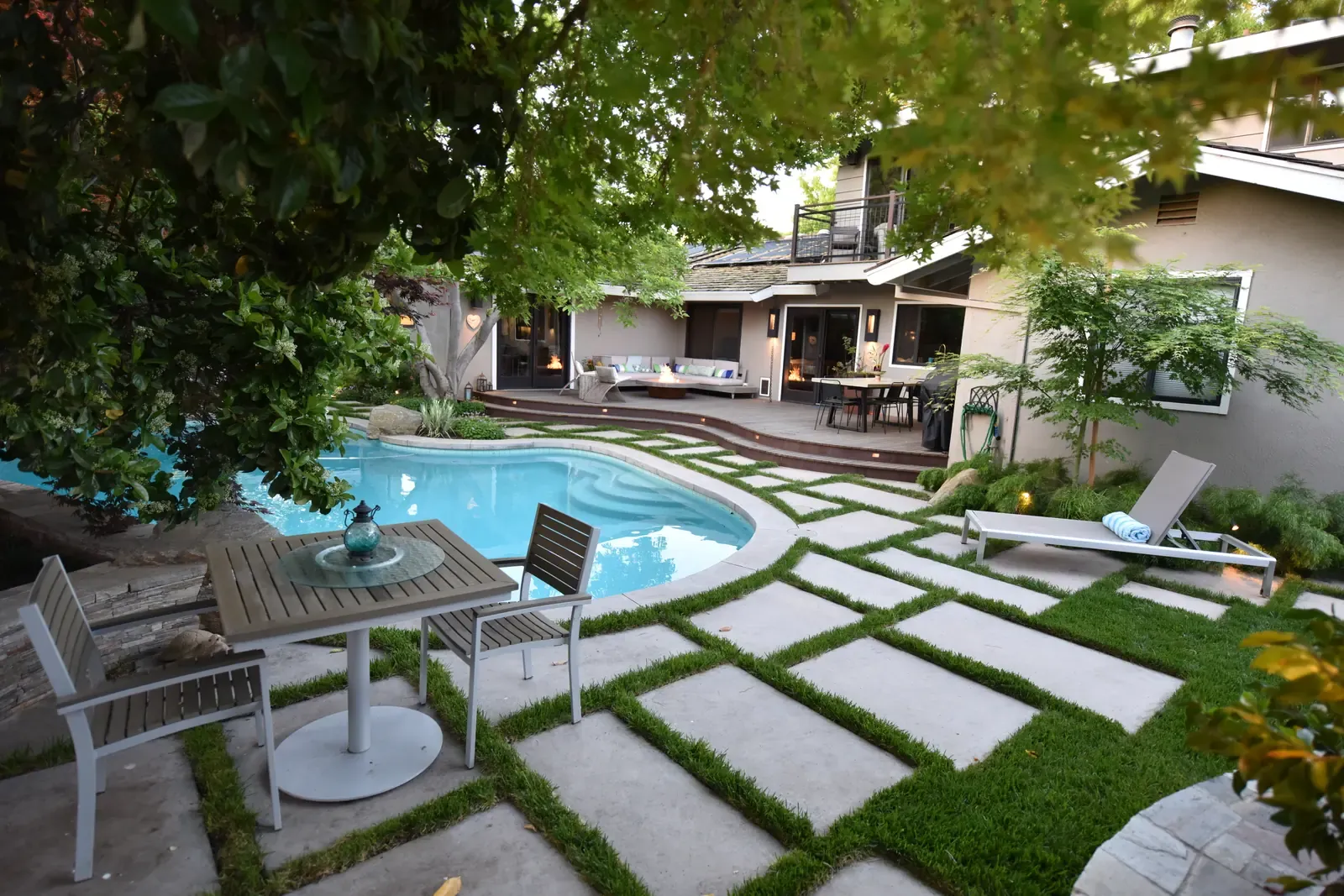 Pool and dining table under a broad shade tree, paving and grass joints throughout