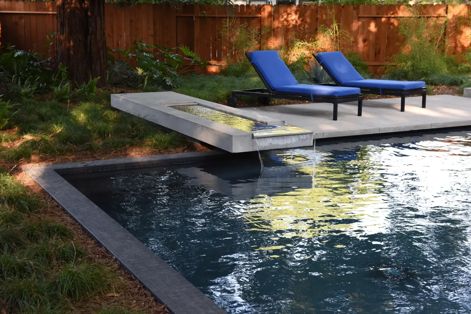 Cantilevered concrete bench projecting over the dark pool, two blue loungers on the paving