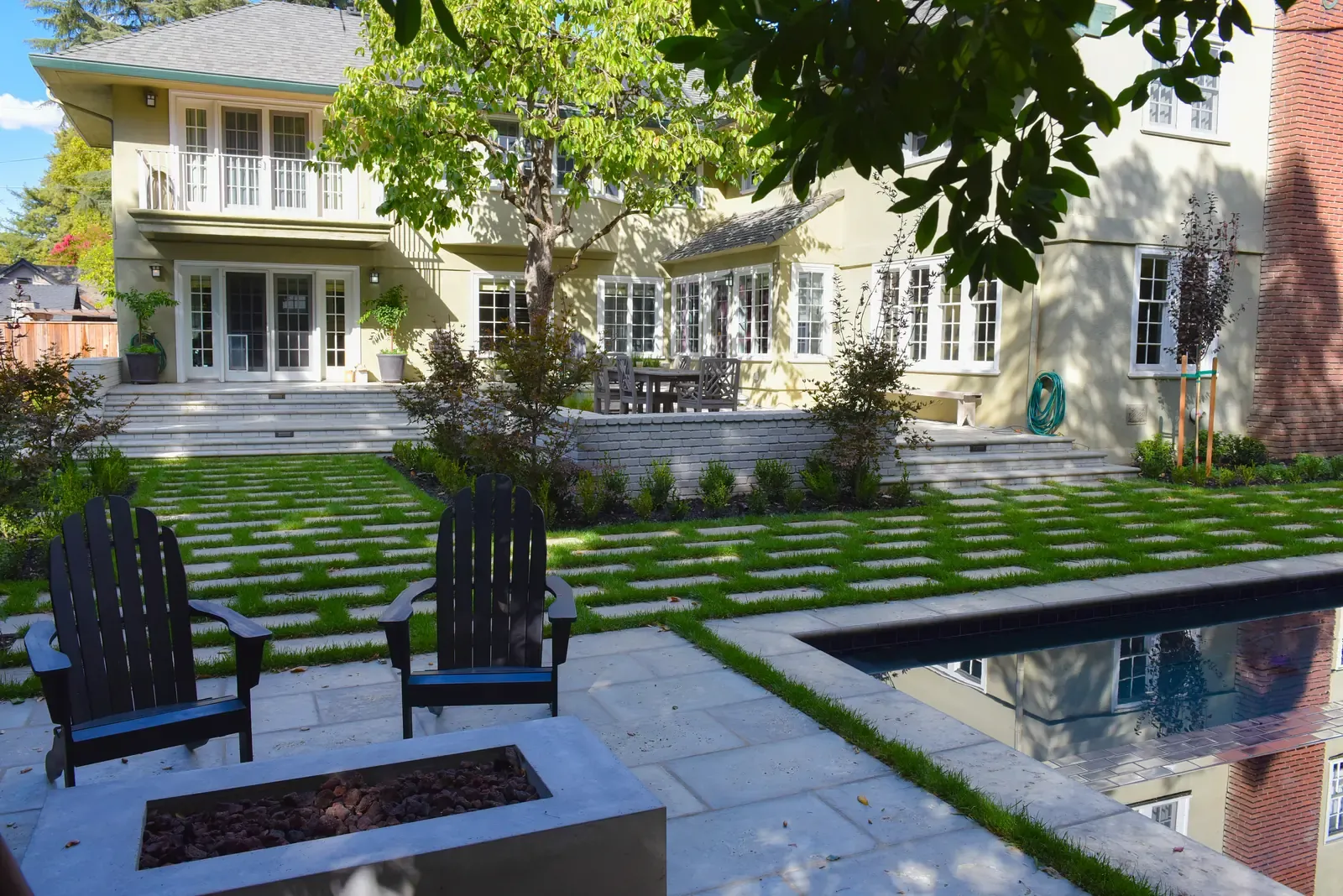 Fire table between the chairs, pool and planting beds running along the house
