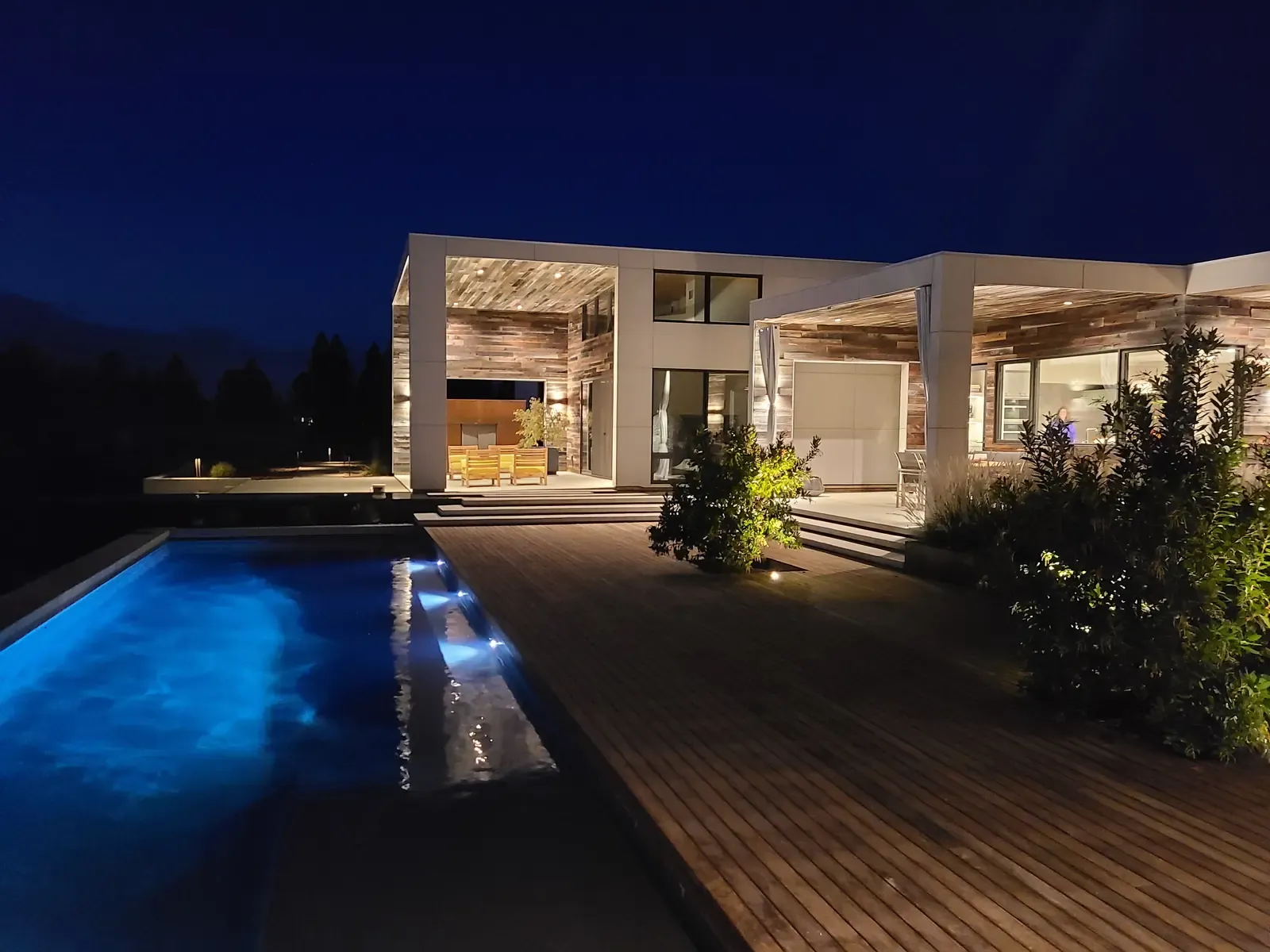 Pool and deck at dusk, the lit interior visible through the glazing