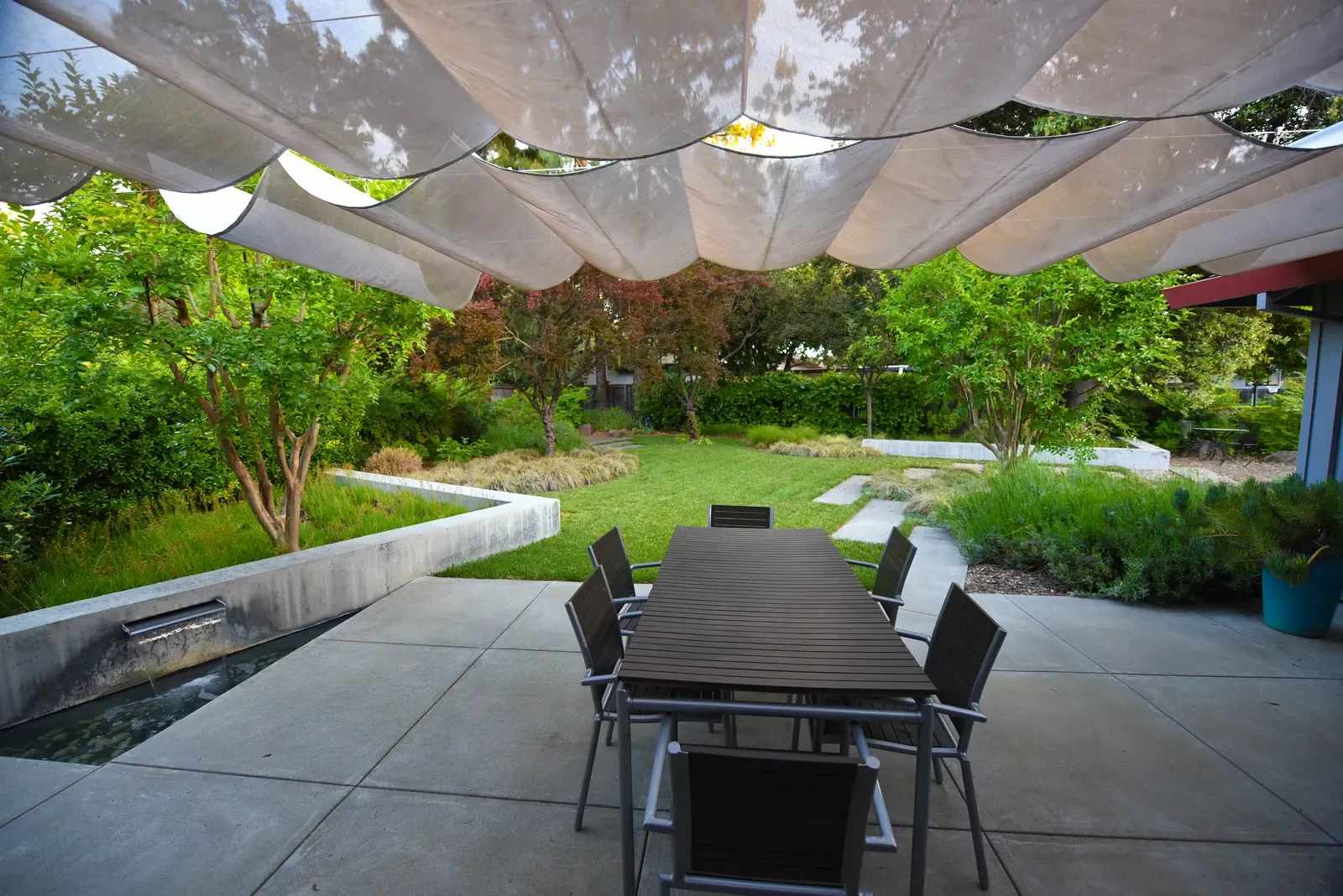 Dining table beneath the shade sails, lawn and paving beyond