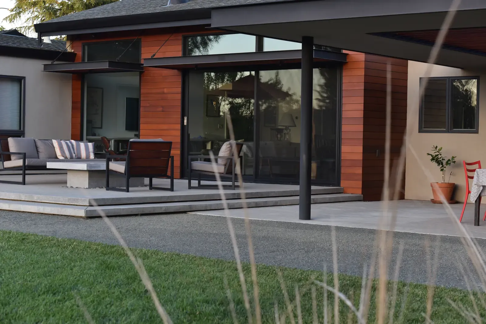 Terrace seating outside the cedar-clad wing, gravel and lawn meeting the paving