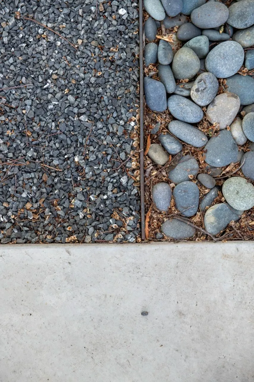 Crushed gravel meeting rounded river stones and a pale concrete edge