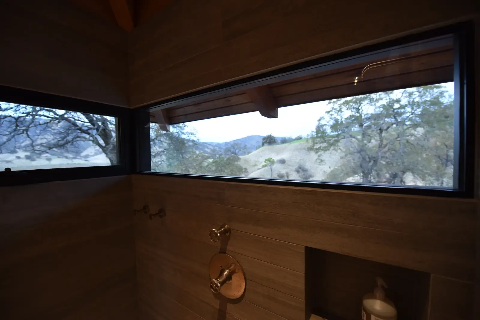 Long horizontal window framing the hillside above a board-formed fireplace