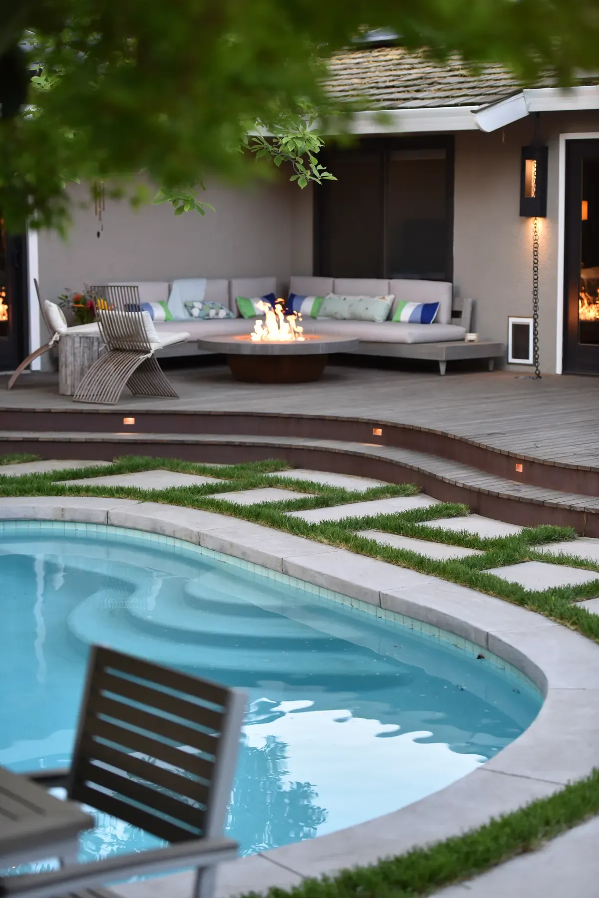 Sofa and fire table on the lit terrace at dusk, pool in the foreground