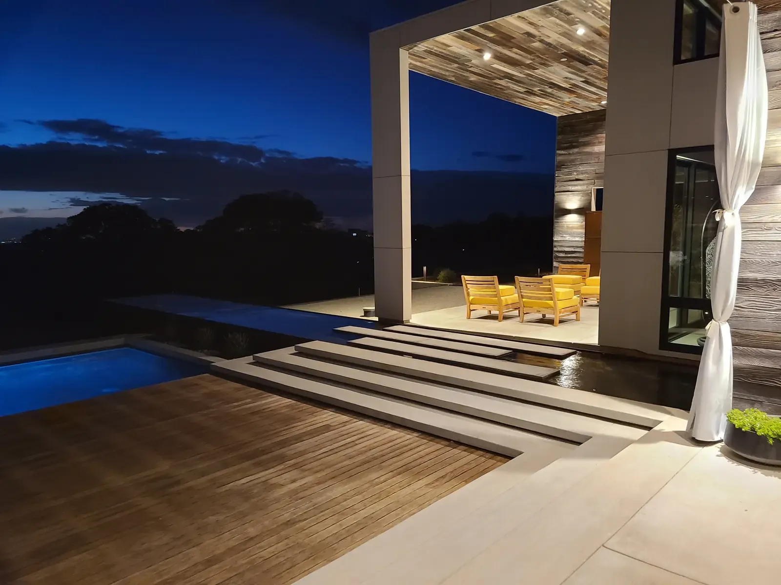 Covered terrace at night, curtains drawn back, broad steps down to the pool
