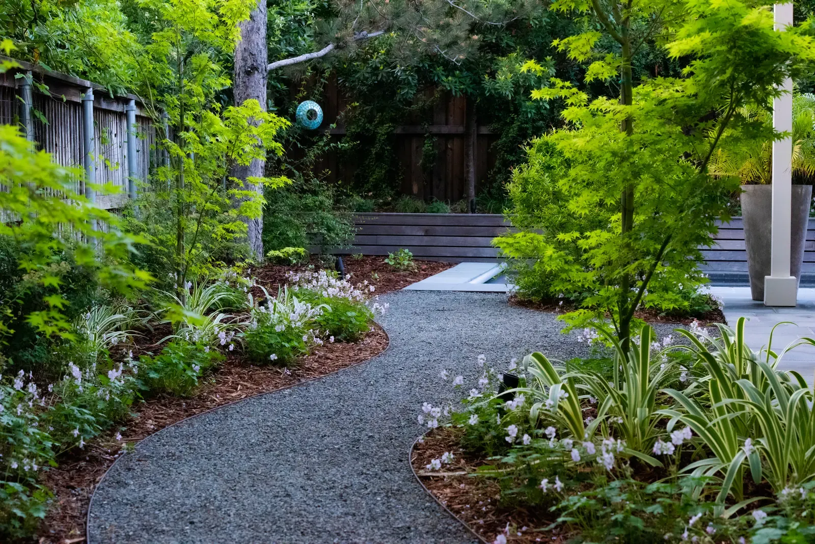 Gravel court enclosed by fencing and planting, small trees throughout