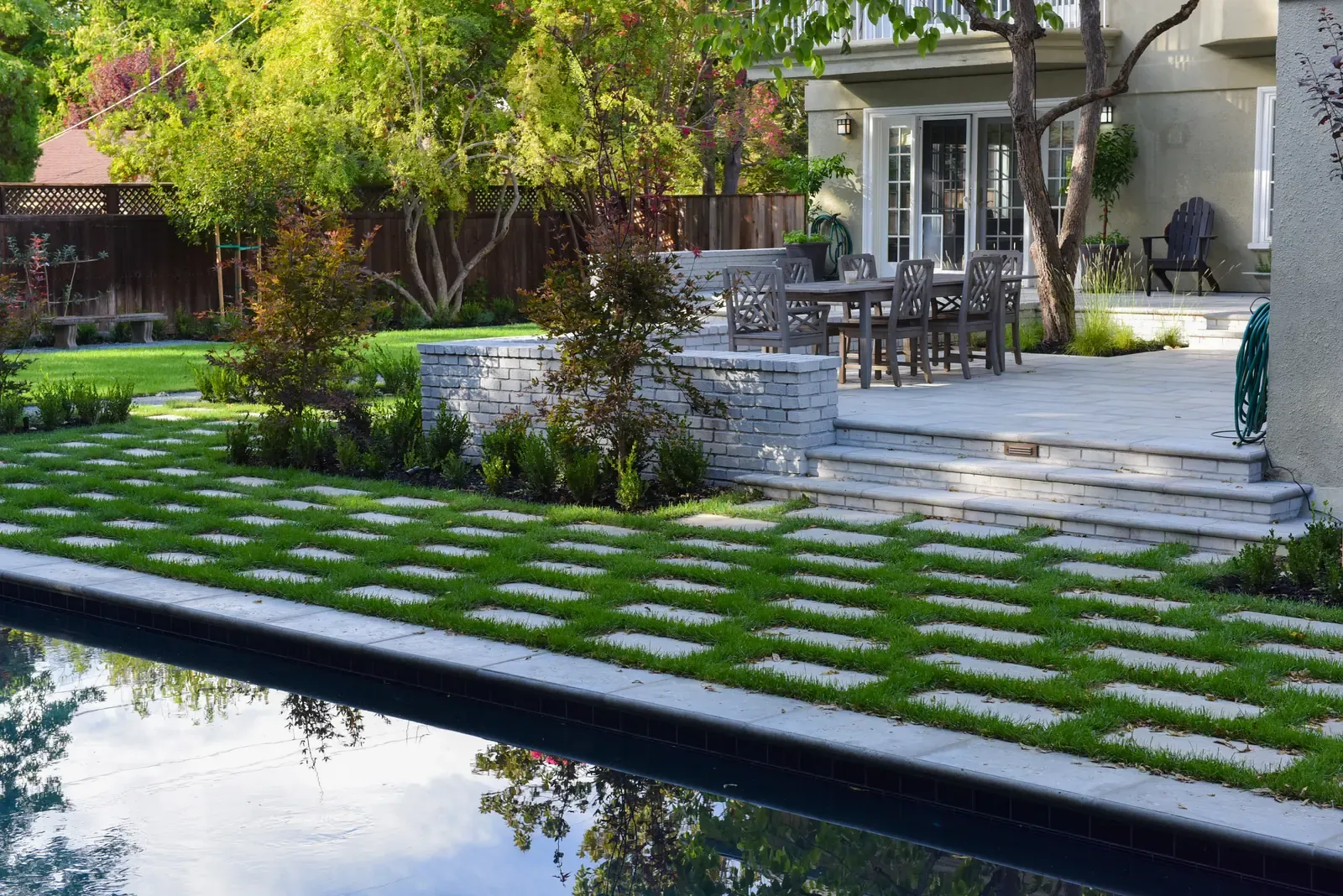 Pool reflecting the trees, dining terrace raised behind a low stone wall