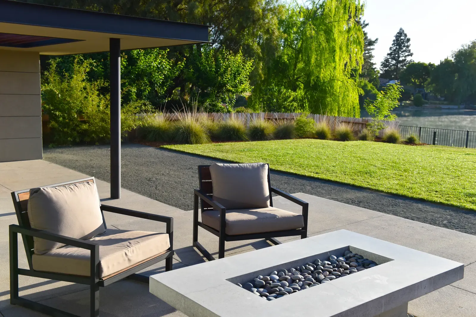 Armchairs beside a concrete fire table on the terrace, lawn and grasses beyond