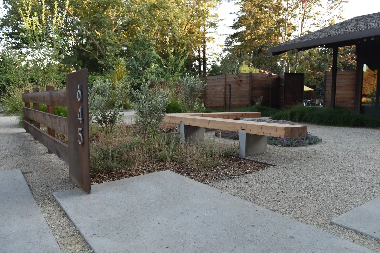 Concrete bench and address panel at the gravel courtyard, covered structure beyond