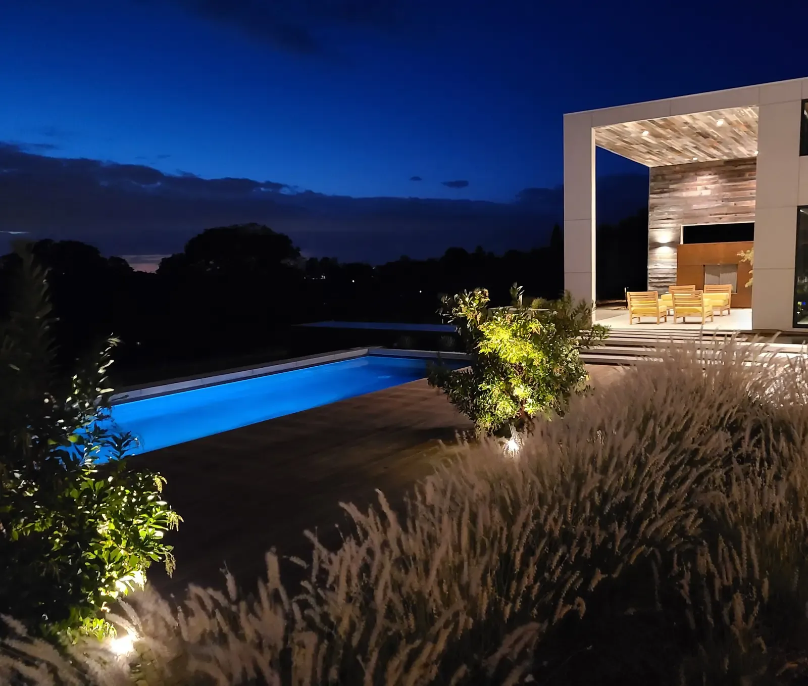 Pool and pavilion lit at dusk, grasses catching the low light