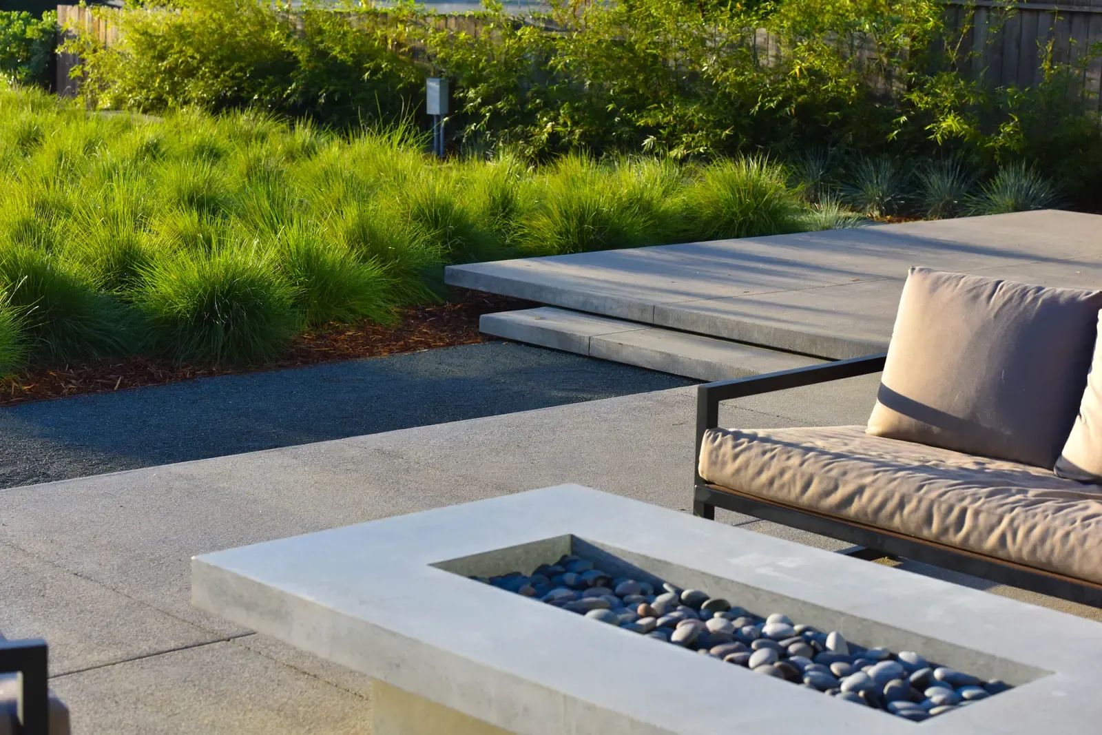 Daybed and concrete fire table set into the paving, planting massed behind