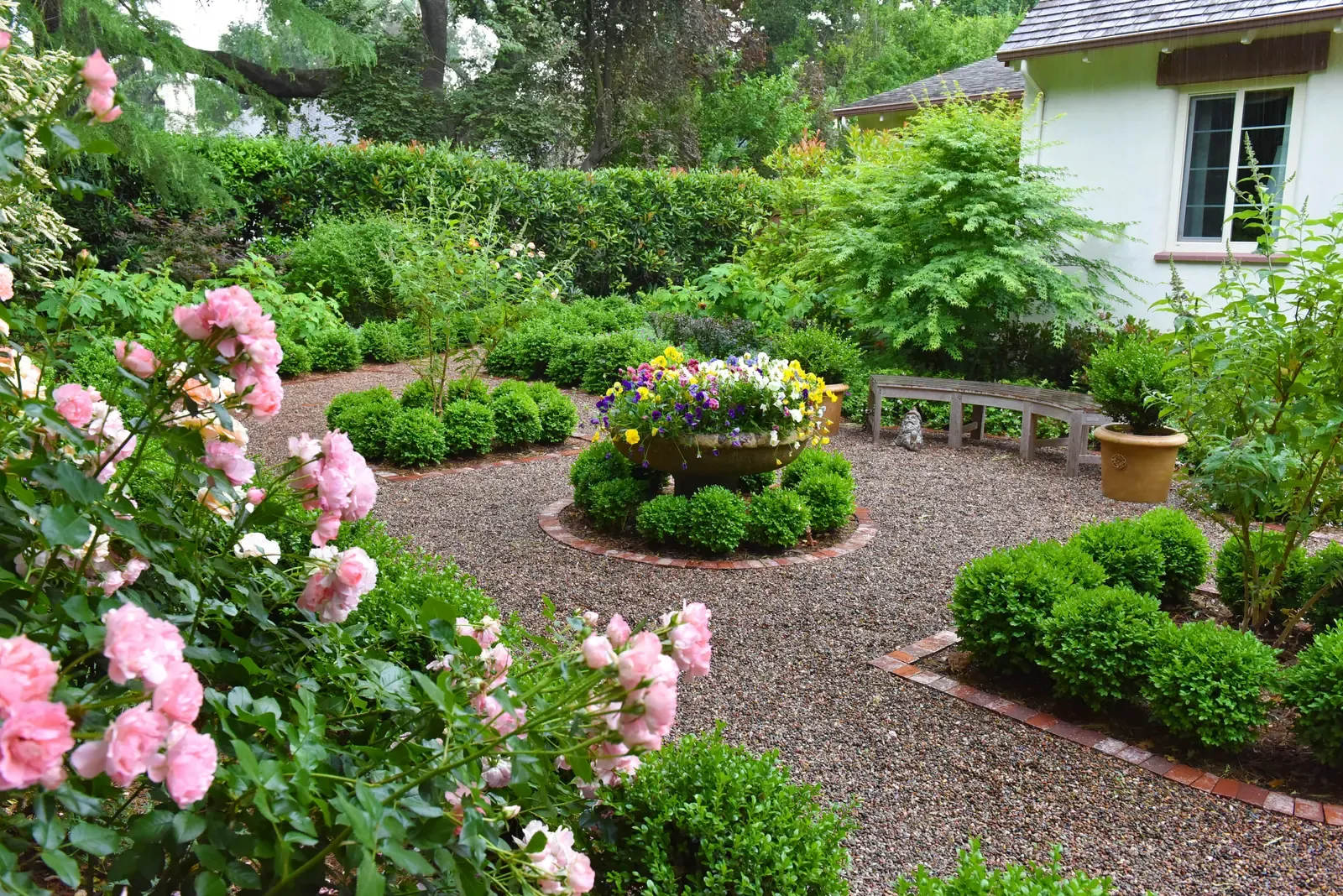 Pink roses in the foreground, circular bed and gravel court beyond