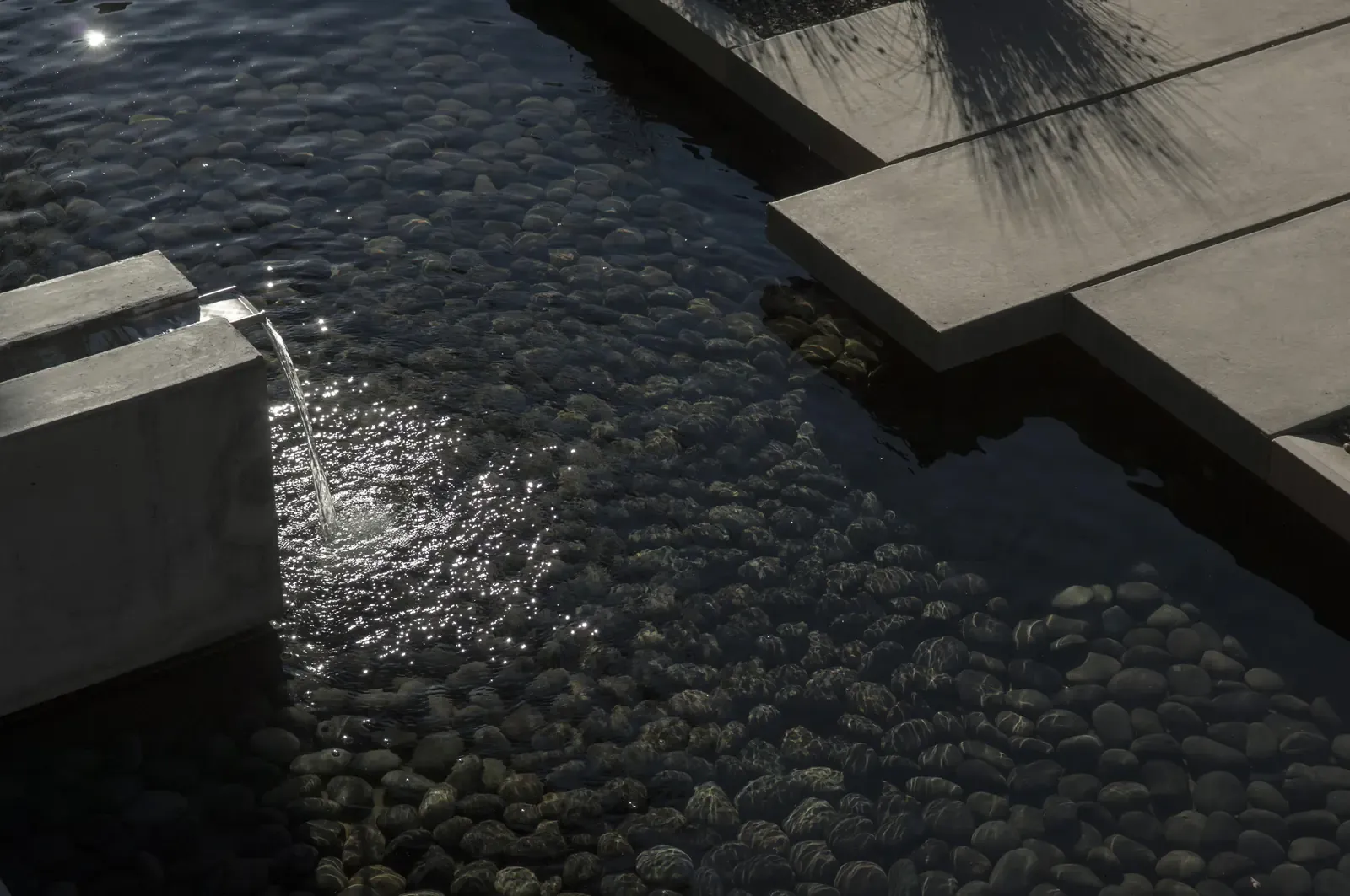 Water spilling from the concrete spout onto the cobble bed