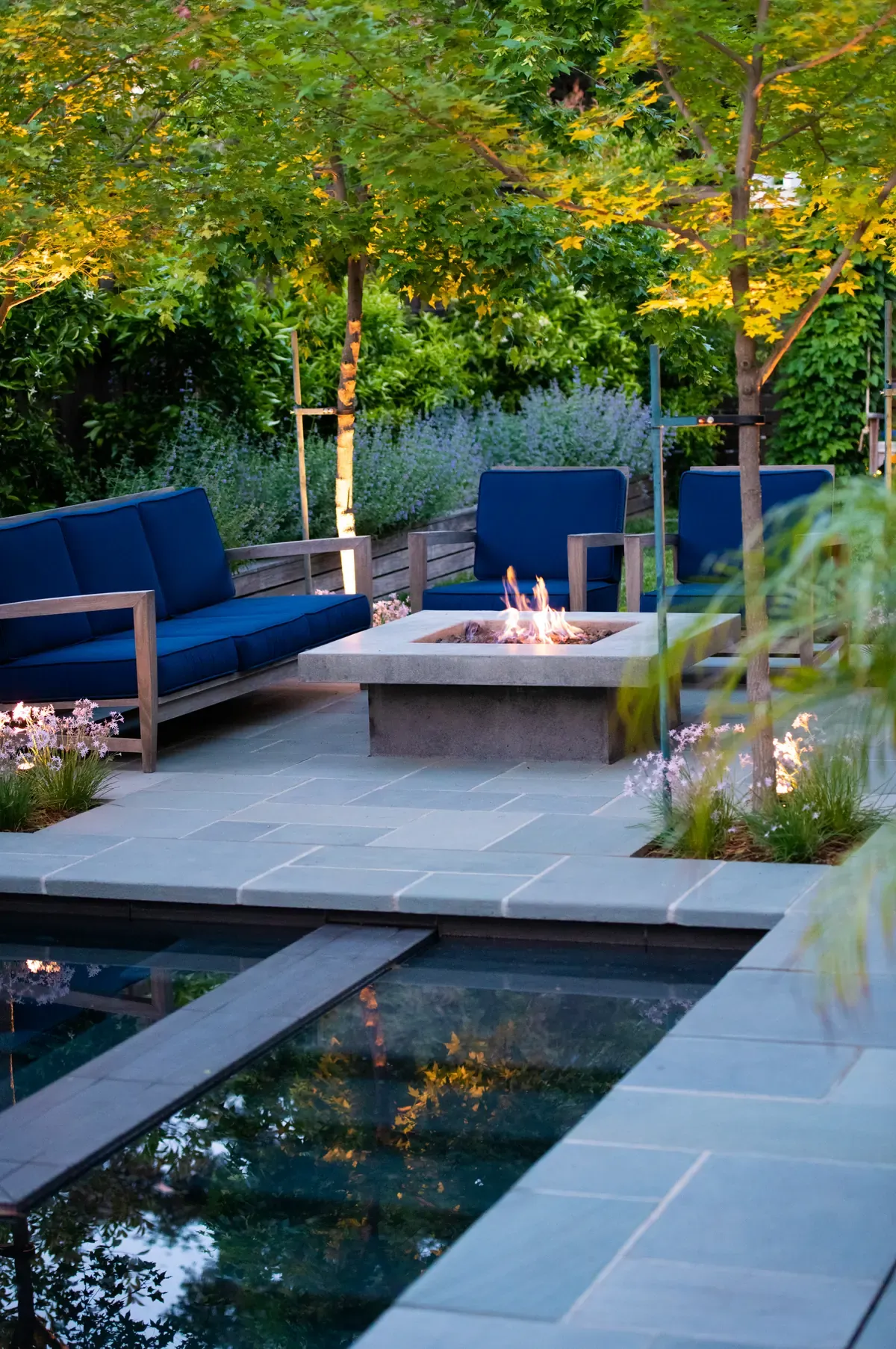 Pool and fire table at dusk, uplit trees behind