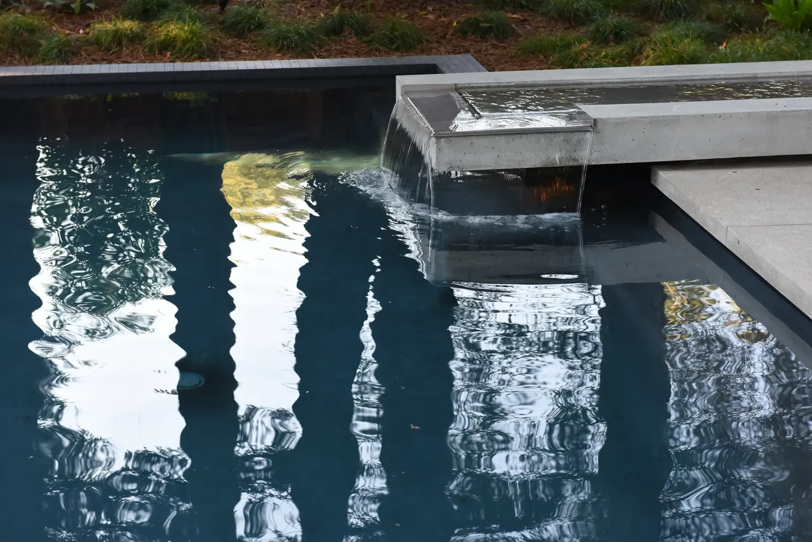 Close view of the water surface, tree trunks reflected beside the concrete spillway