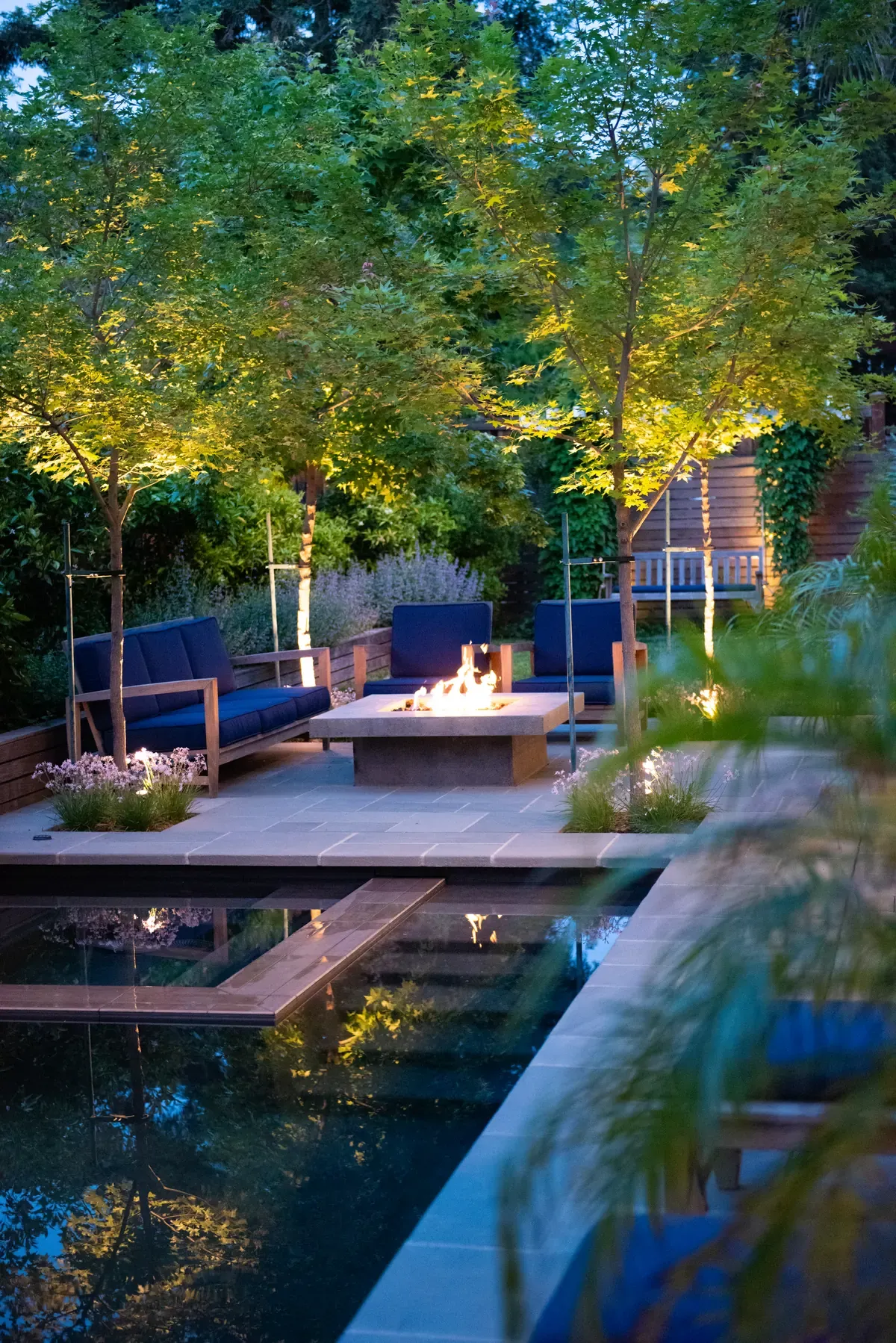 Fire alight beside the pool at dusk, trees lit overhead