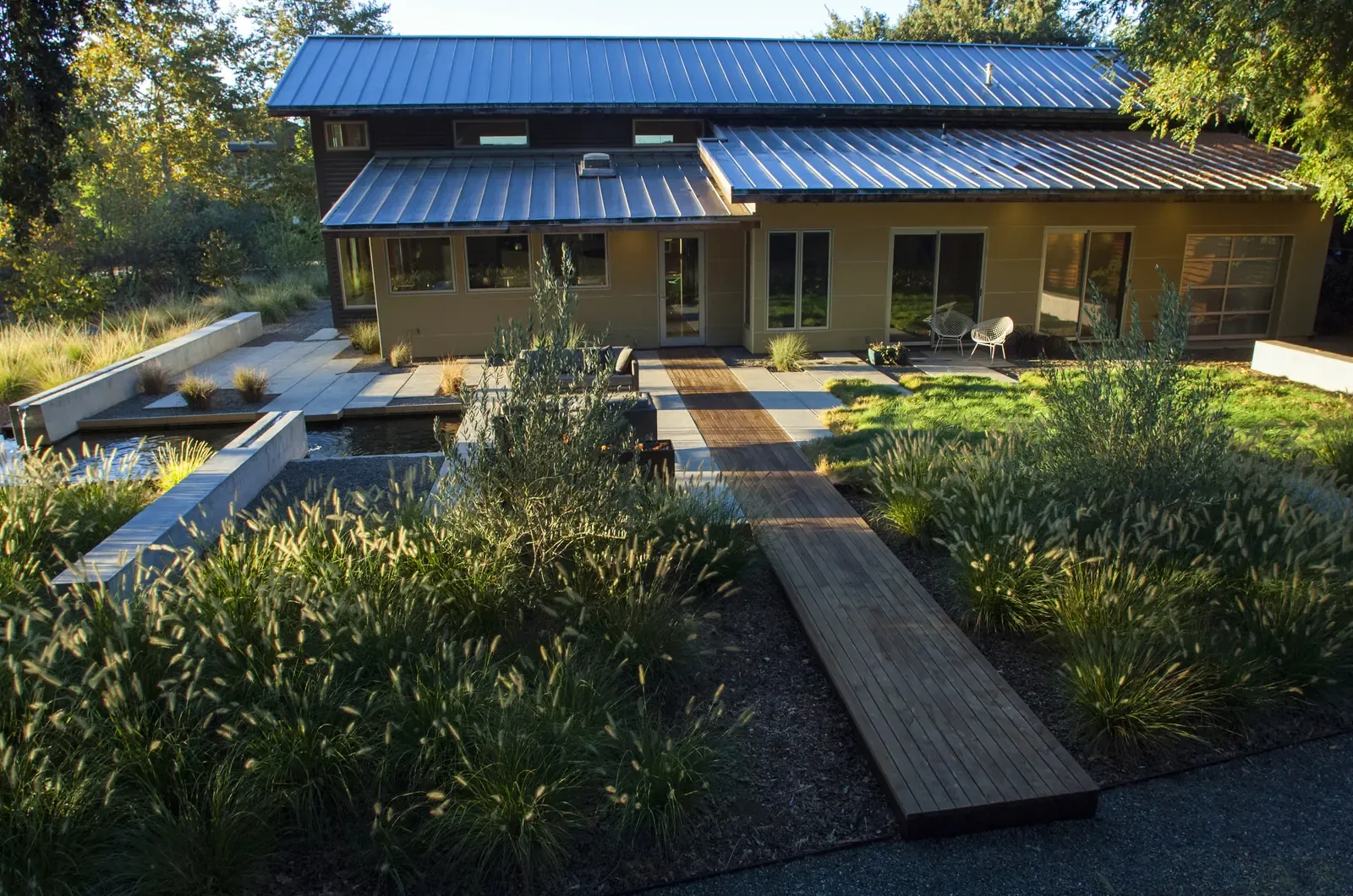 The house with its blue roof seen across the planting, boardwalk crossing the water