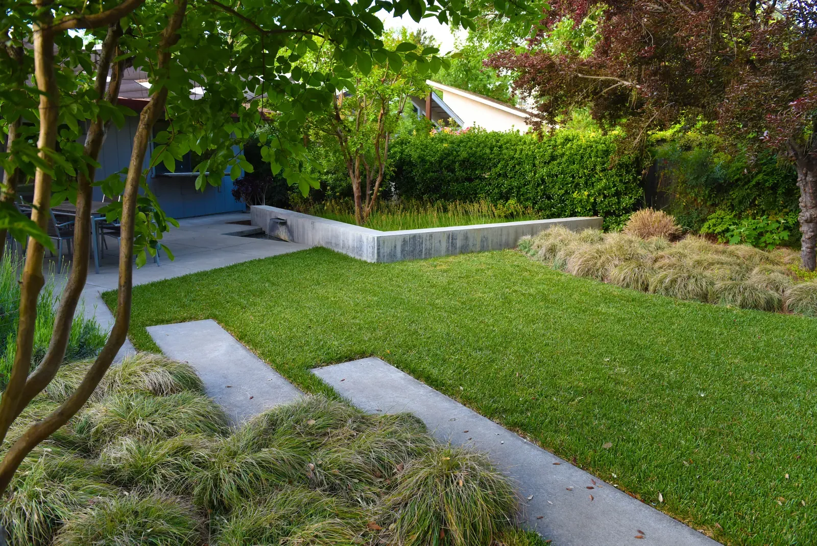 Lawn edged by a low concrete wall, stepping stones running through