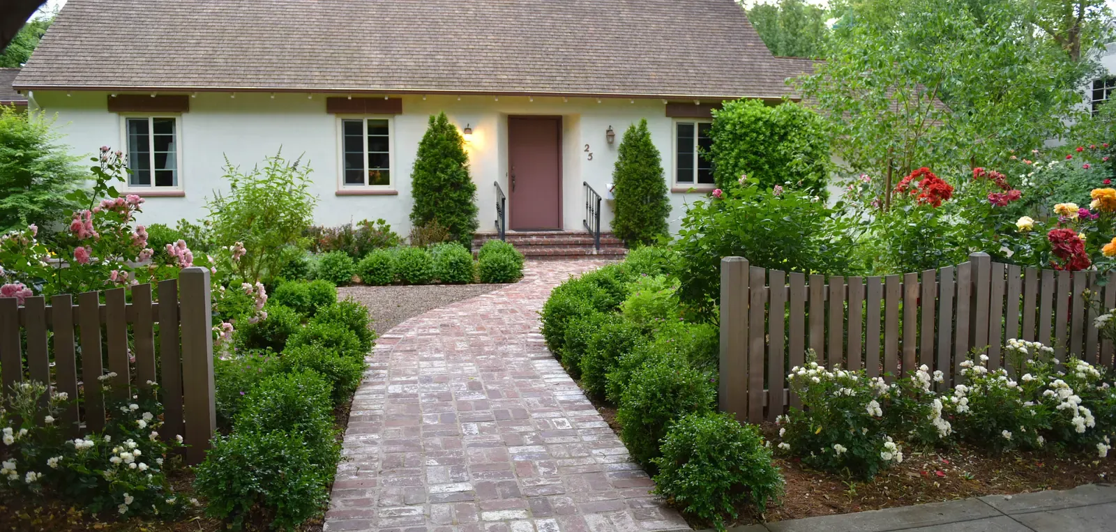 Brick walk leading to the front door between clipped shrubs