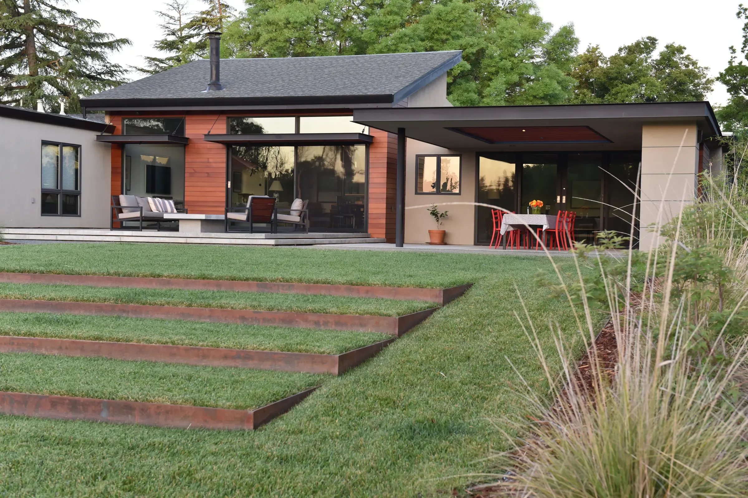 Broad weathering-steel steps stepping down the lawn to the house at dusk, grasses at the edge