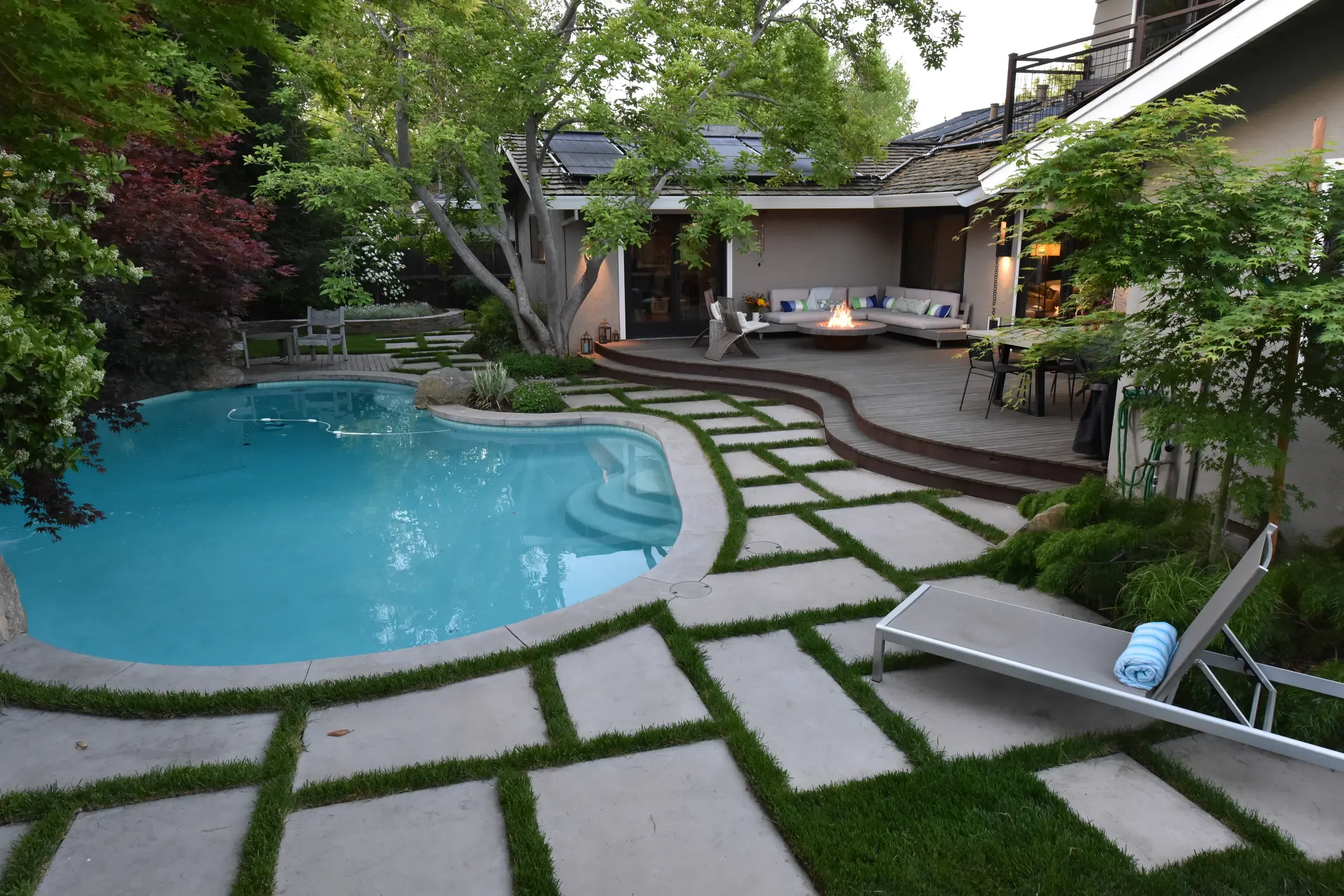 Curved pool edged with concrete pavers set in grass joints, house and covered terrace beyond