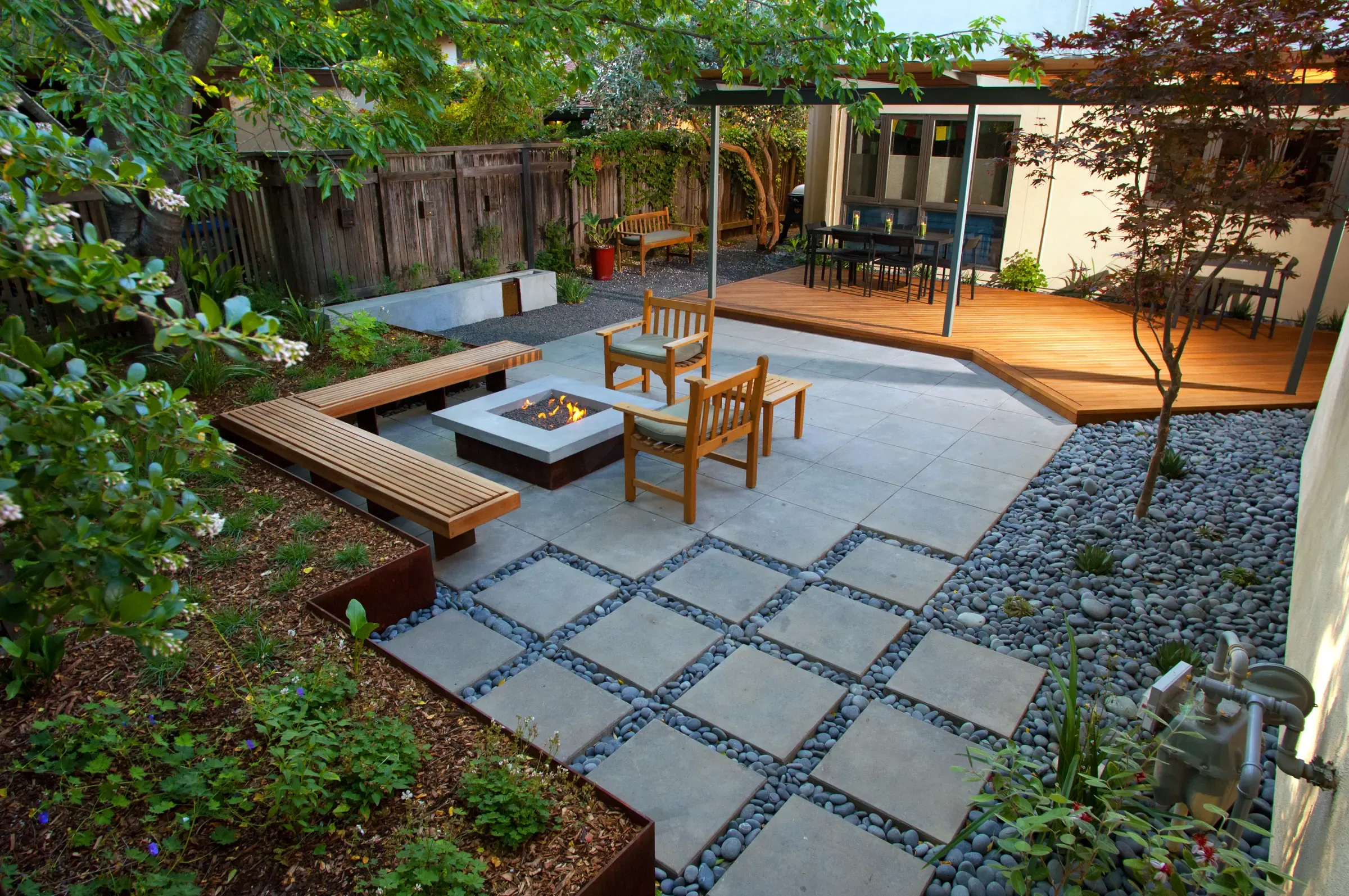 Paved terrace with a fire pit, timber bench and dining area against a board fence