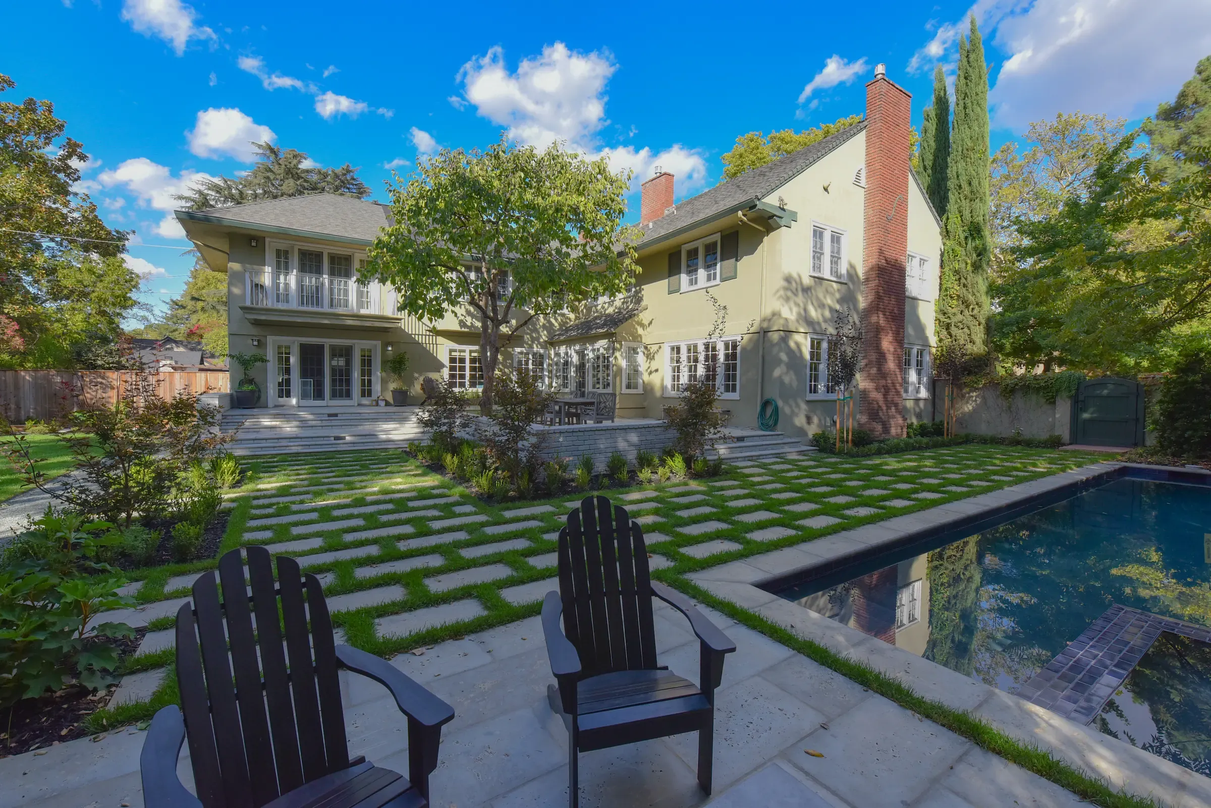 Pool and bluestone pavers set in grass joints, two dark Adirondack chairs facing the house