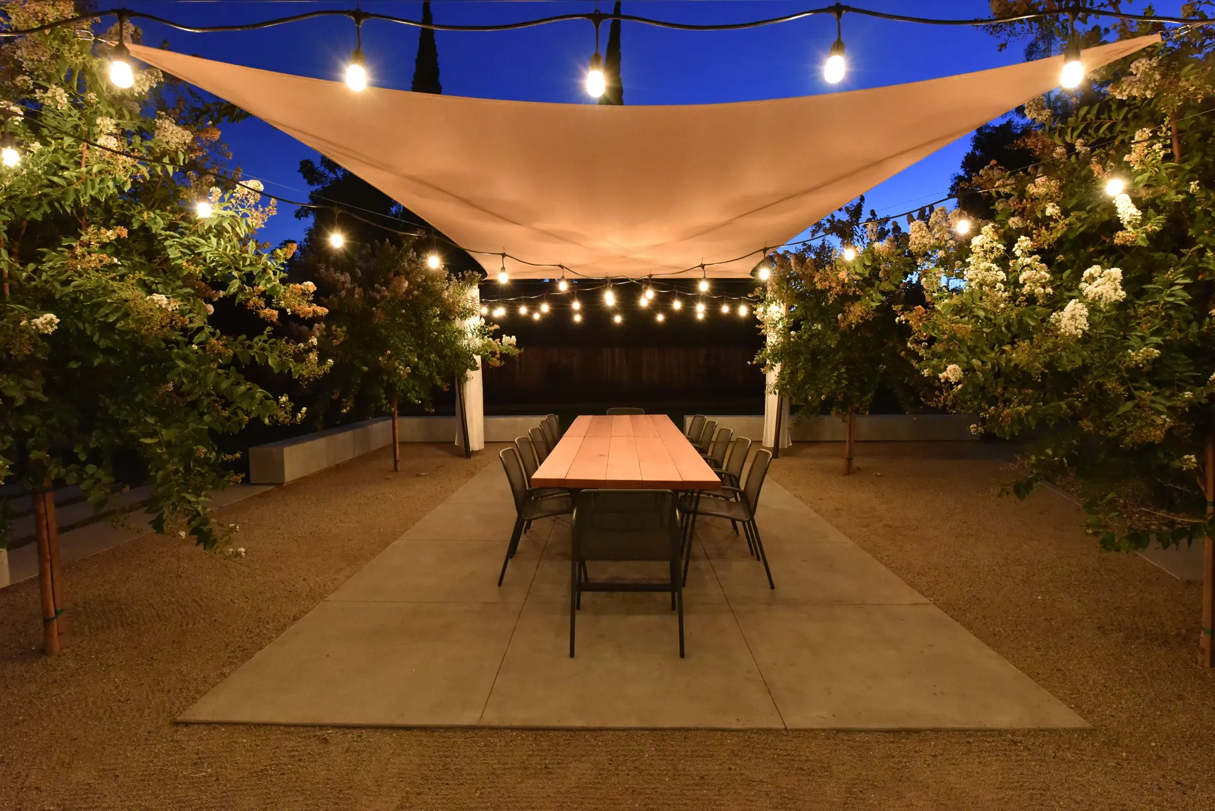 Shade sail over a long dining table at night, festoon lights strung through the trees
